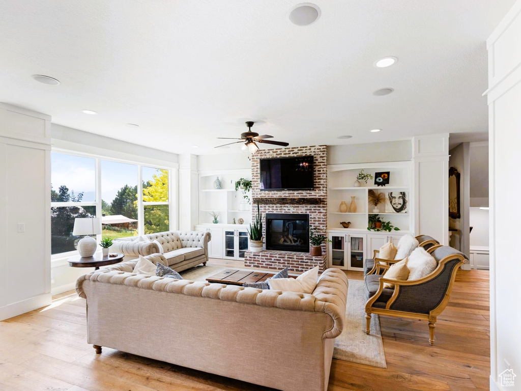Living room with built in shelves, light wood-style floors, a brick fireplace, and ceiling fan