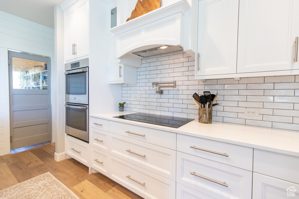 Kitchen featuring stainless steel double oven, light countertops, light wood-style floors, white cabinetry, and black electric cooktop