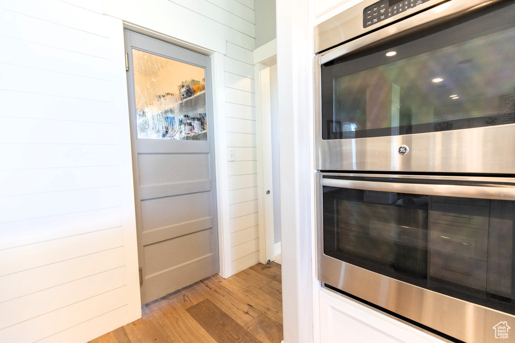 Kitchen featuring white cabinetry, light wood-style flooring, wooden walls, and stainless steel double oven
