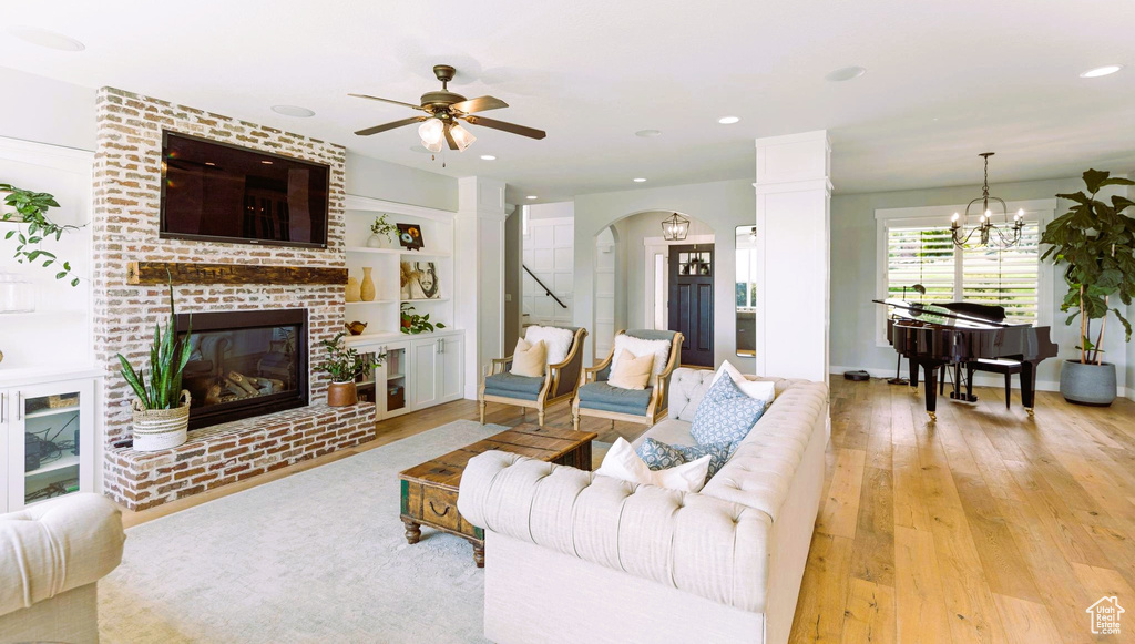 Living room with ceiling fan with notable chandelier, a brick fireplace, recessed lighting, and light wood-style flooring