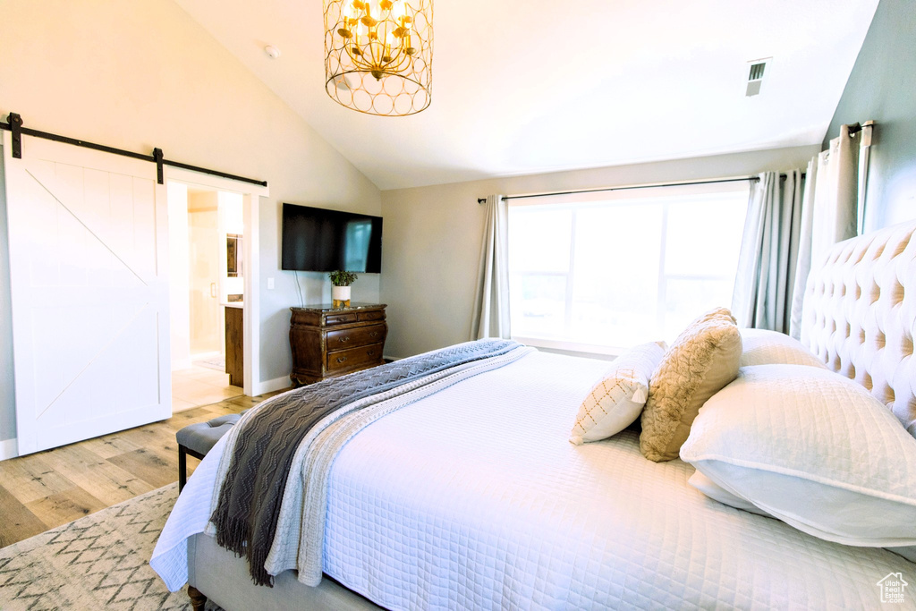 Bedroom featuring visible vents, lofted ceiling, a barn door, an inviting chandelier, and wood finished floors