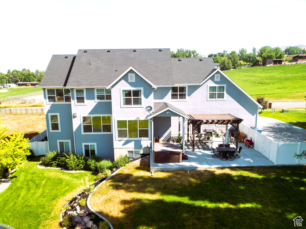 Back of house featuring a lawn, a pergola, a patio, a fenced backyard, and a hot tub