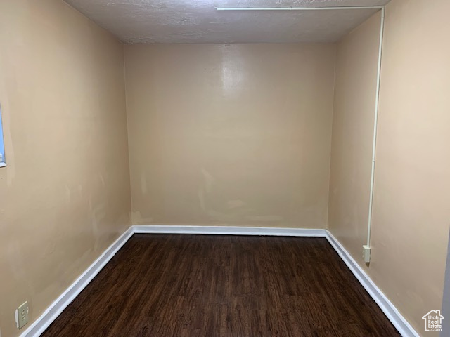 Unfurnished room featuring baseboards, dark wood-style flooring, and a textured ceiling