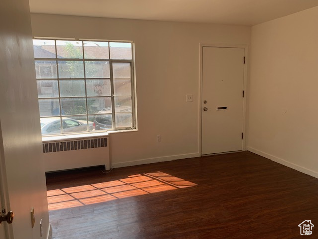 Empty room featuring baseboards, wood finished floors, and radiator heating unit