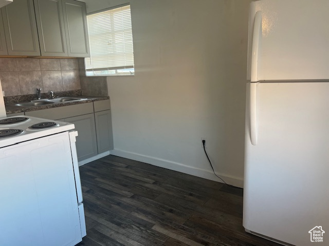 Kitchen with white appliances, baseboards, dark wood-style flooring, a sink, and decorative backsplash