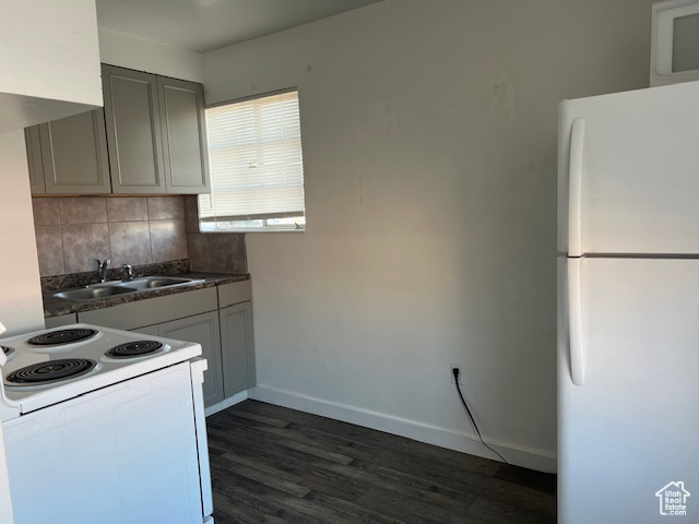 Kitchen with white appliances, baseboards, dark wood-style flooring, a sink, and decorative backsplash