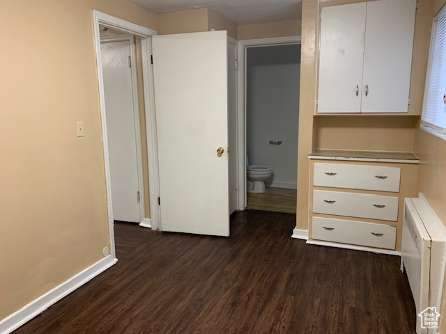 Unfurnished bedroom with radiator, baseboards, and dark wood-style flooring