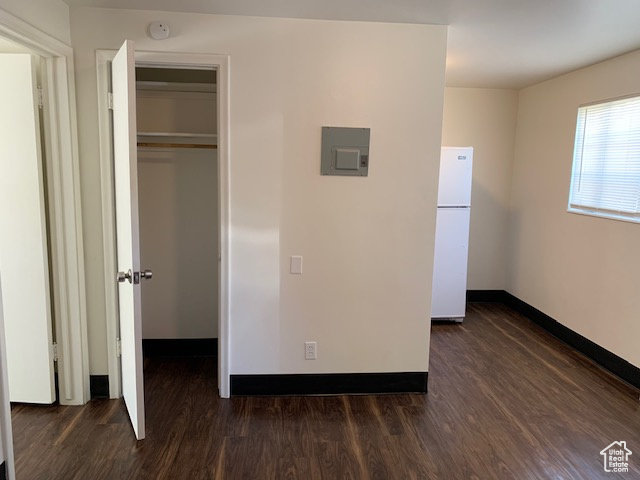 Unfurnished bedroom with a closet, baseboards, dark wood-style floors, and freestanding refrigerator