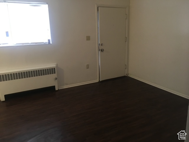 Spare room with baseboards, dark wood-style flooring, and radiator heating unit