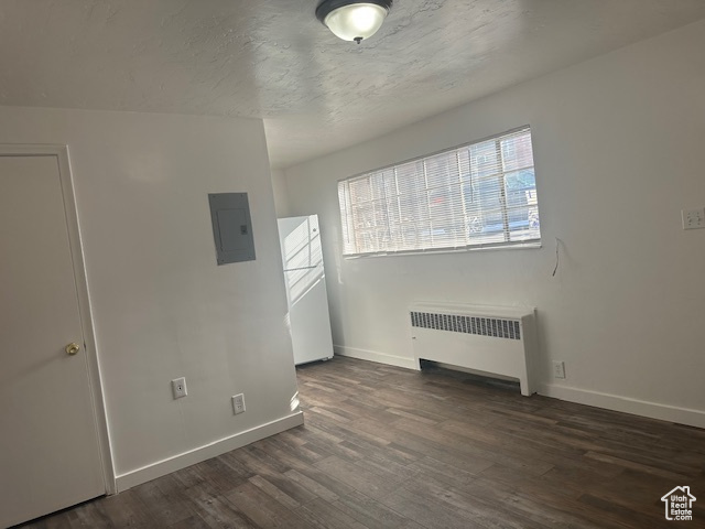 Spare room featuring electric panel, baseboards, wood finished floors, and radiator heating unit