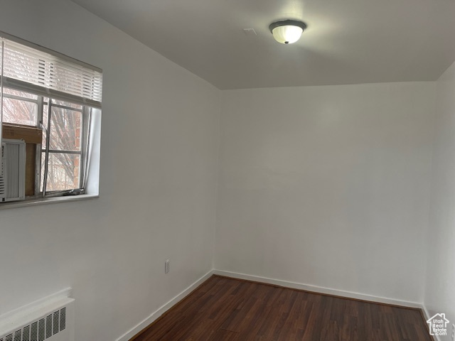 Empty room with baseboards, dark wood-style flooring, and radiator heating unit