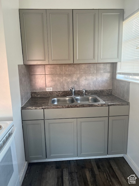 Kitchen featuring dark wood-style flooring, gray cabinetry, decorative backsplash, a sink, and dark countertops
