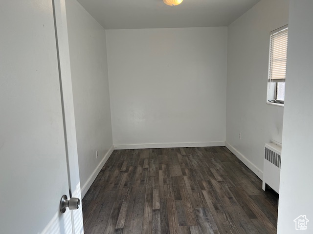 Unfurnished room with baseboards, radiator, and dark wood-style floors