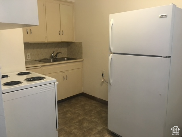 Kitchen with a sink, tasteful backsplash, white appliances, dark floors, and light countertops
