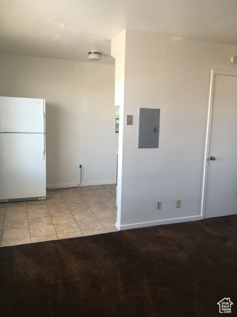 Interior space with electric panel, tile patterned floors, freestanding refrigerator, and carpet