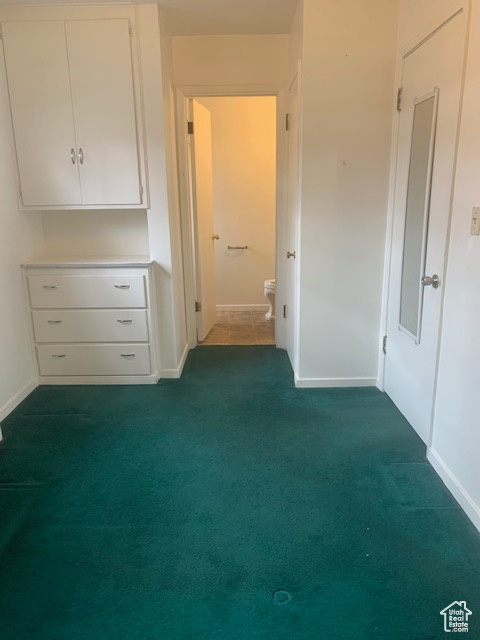 Unfurnished bedroom featuring connected bathroom, baseboards, and dark colored carpet