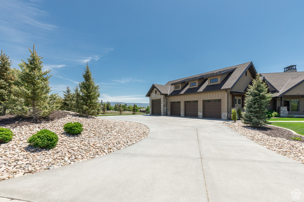 View of front of property featuring board and batten siding, concrete driveway, stone siding, and a shingled roof