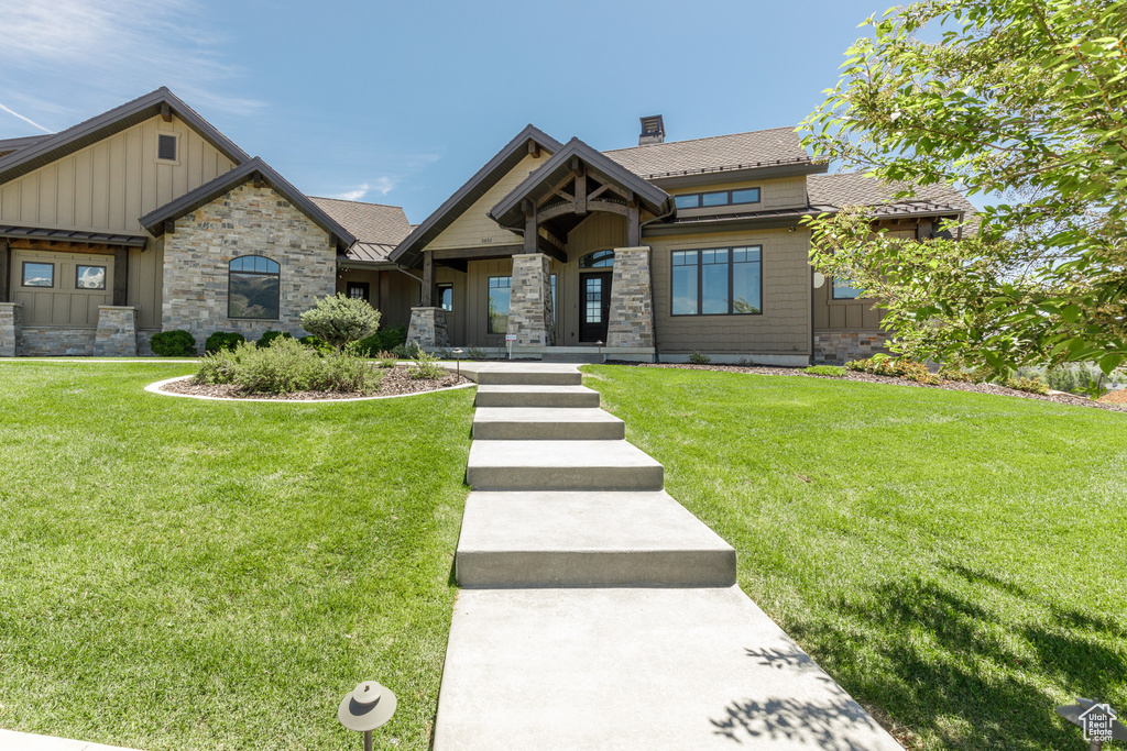 View of front of home featuring board and batten siding, a front lawn, a chimney, and stone siding