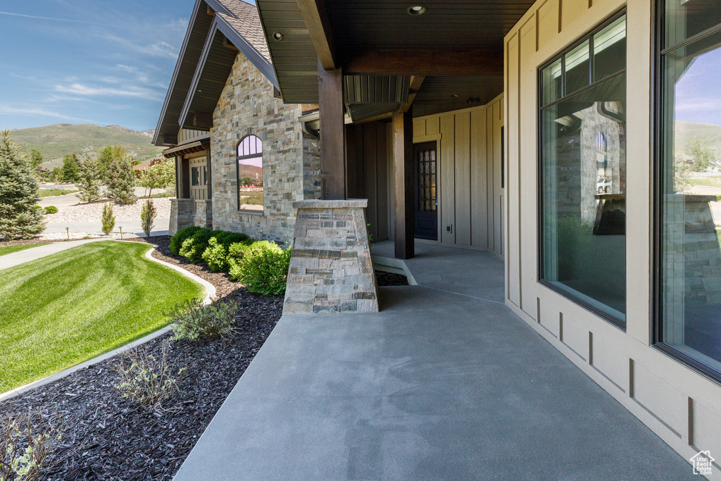 View of exterior entry featuring board and batten siding, a mountain view, stone siding, and a lawn