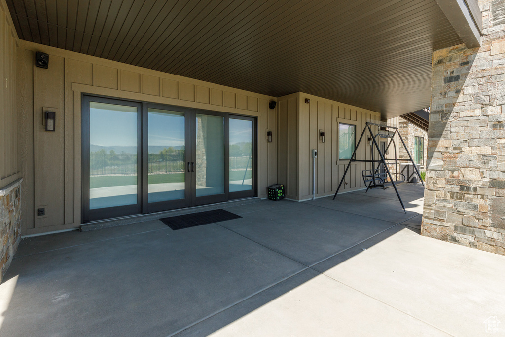 Entrance to property with a patio, board and batten siding, stone siding, and french doors