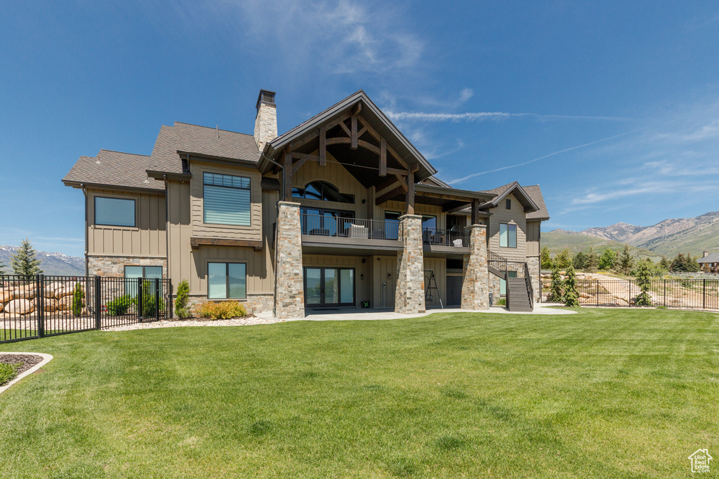 Back of house featuring a balcony, stone siding, board and batten siding, a chimney, and a mountain view