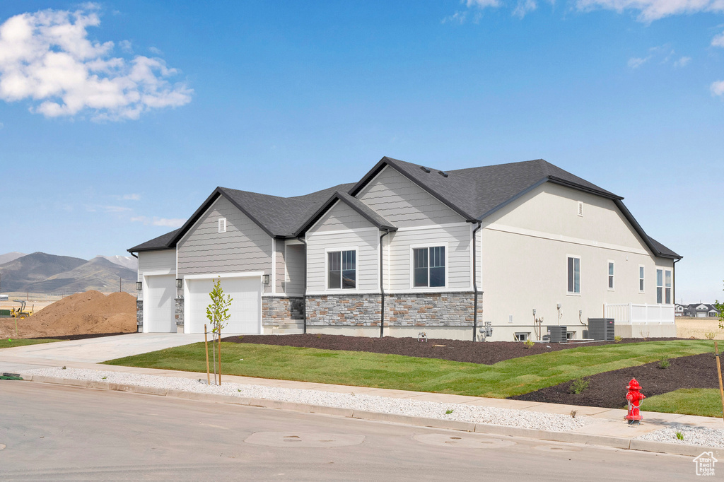 View of front of home featuring concrete driveway, central AC unit, stone siding, a front lawn, and a garage