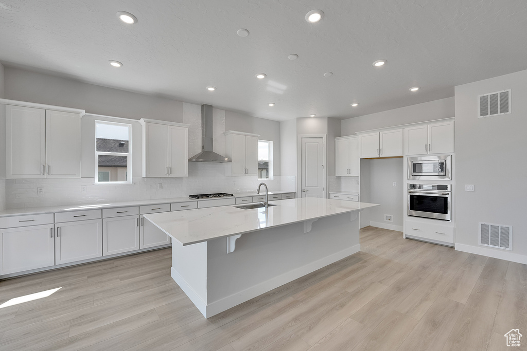 Kitchen with wall chimney exhaust hood, appliances with stainless steel finishes, a sink, white cabinetry, and recessed lighting