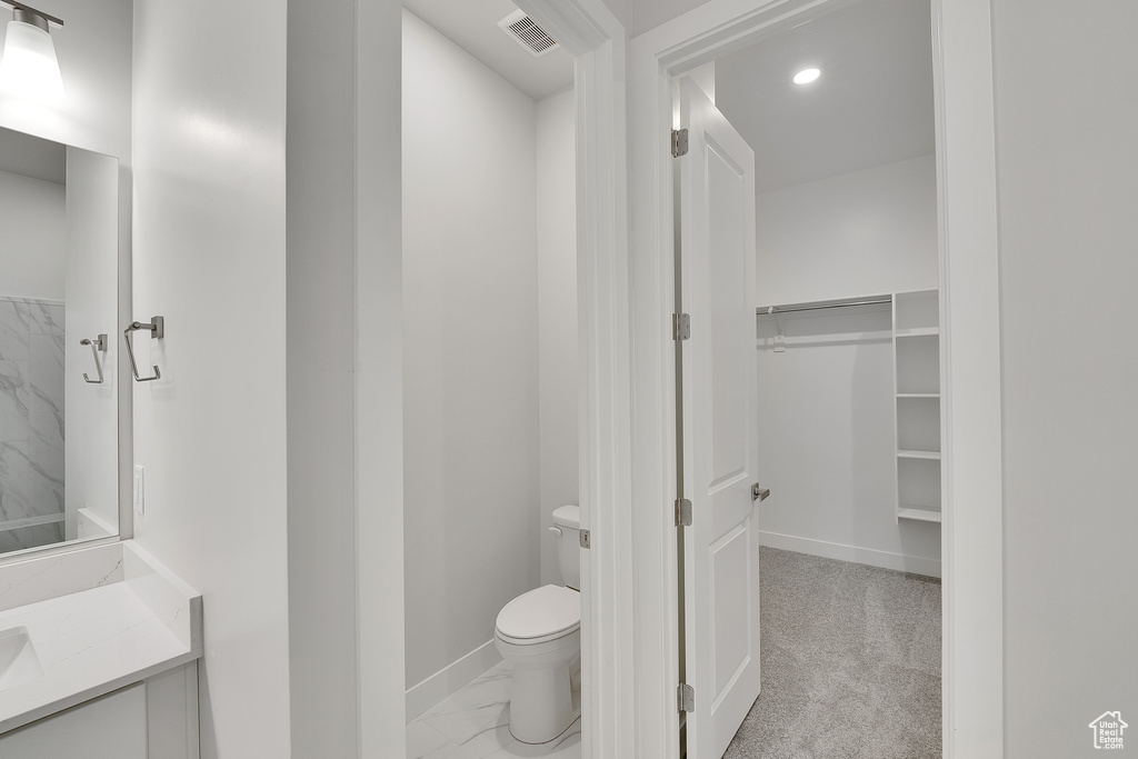 Bathroom featuring a walk in closet, vanity, marble look tile flooring, toilet, and baseboards