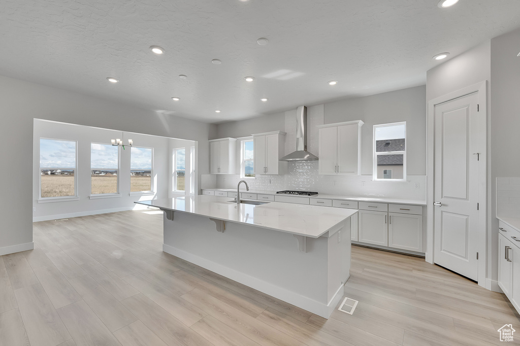 Kitchen featuring wall chimney exhaust hood, a sink, backsplash, a chandelier, and recessed lighting