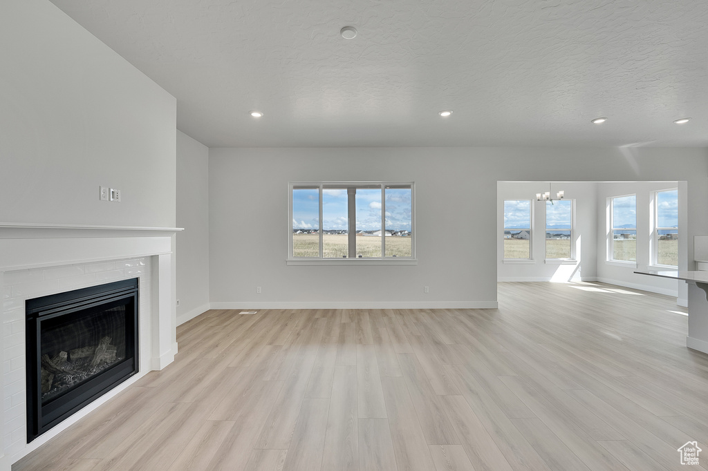 Unfurnished living room featuring a chandelier, a fireplace, light wood-style flooring, recessed lighting, and baseboards