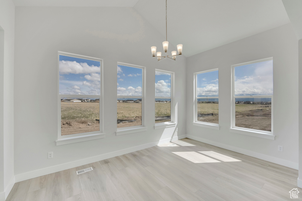 Unfurnished dining area with a chandelier, healthy amount of natural light, light wood-style flooring, lofted ceiling, and baseboards