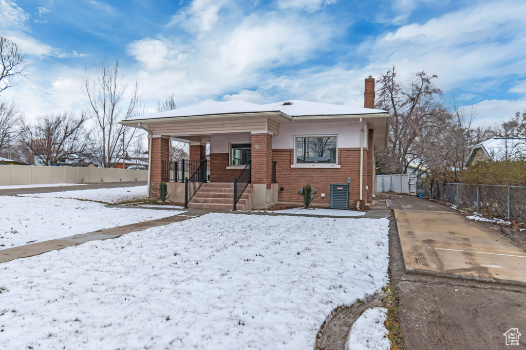 View of front facade with fence, covered porch, brick siding, and a chimney