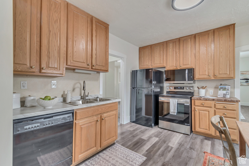 Kitchen featuring a sink, light wood-style floors, black appliances, and light countertops