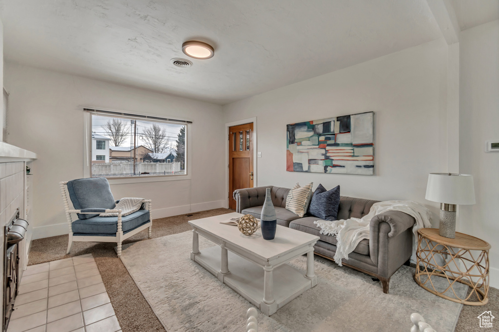 Living room with a tiled fireplace, visible vents, light carpet, and baseboards