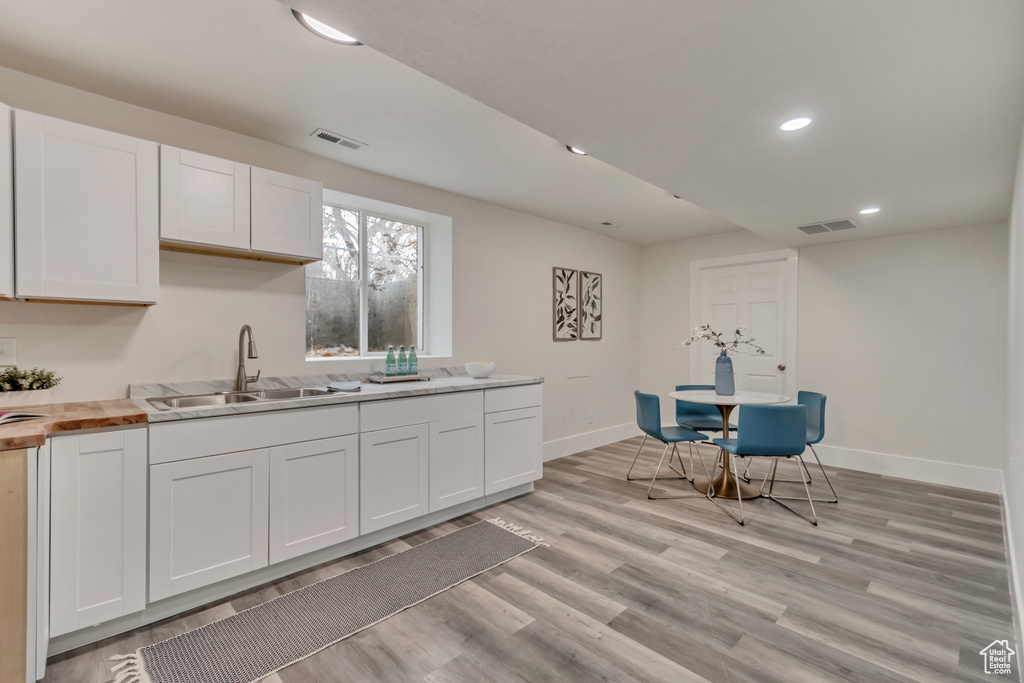 Kitchen with white cabinets, light wood-style floors, visible vents, and a sink