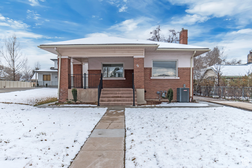 Snow covered property featuring brick siding, central air condition unit, a chimney, and fence