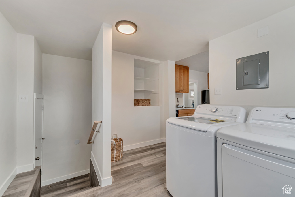 Clothes washing area with electric panel, independent washer and dryer, light wood finished floors, and baseboards