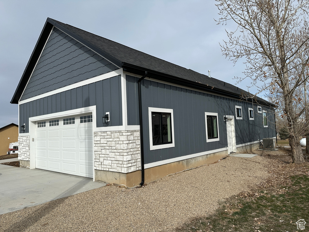 View of home\'s exterior featuring stone siding, central AC unit, concrete driveway, and a garage