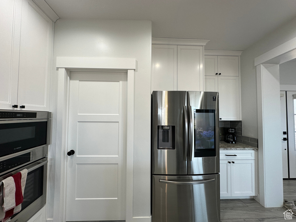 Kitchen featuring white cabinets, light stone countertops, tasteful backsplash, and appliances with stainless steel finishes