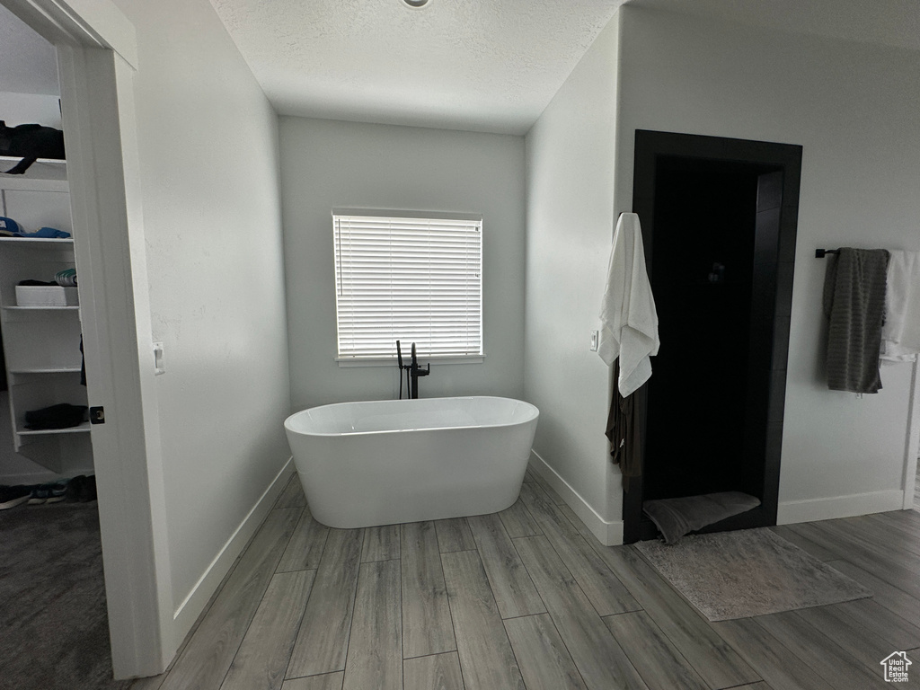 Bathroom featuring a freestanding tub, wood finished floors, baseboards, and a textured ceiling