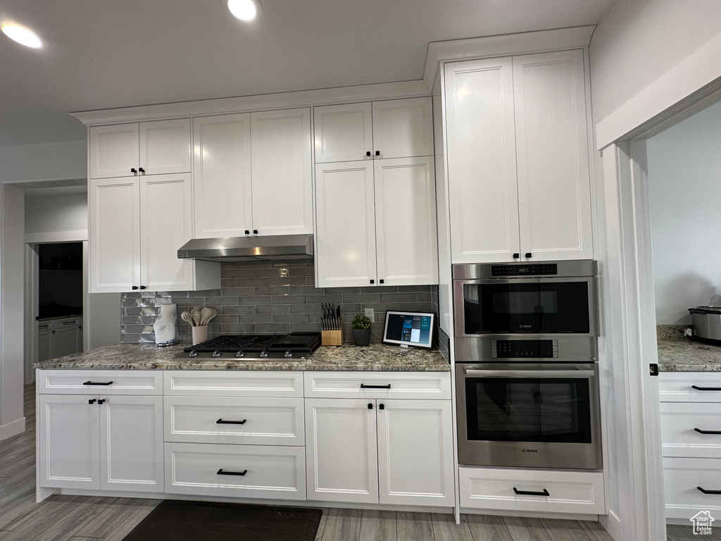 Kitchen featuring under cabinet range hood, light stone countertops, stainless steel appliances, and tasteful backsplash