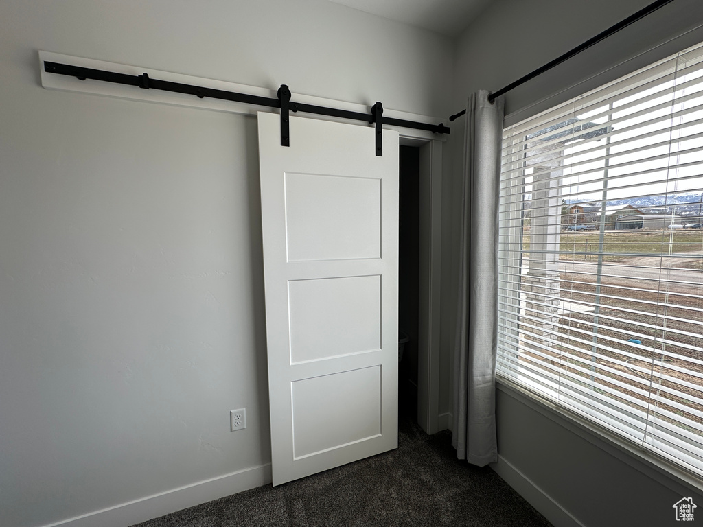 Unfurnished bedroom with a barn door, baseboards, and dark colored carpet