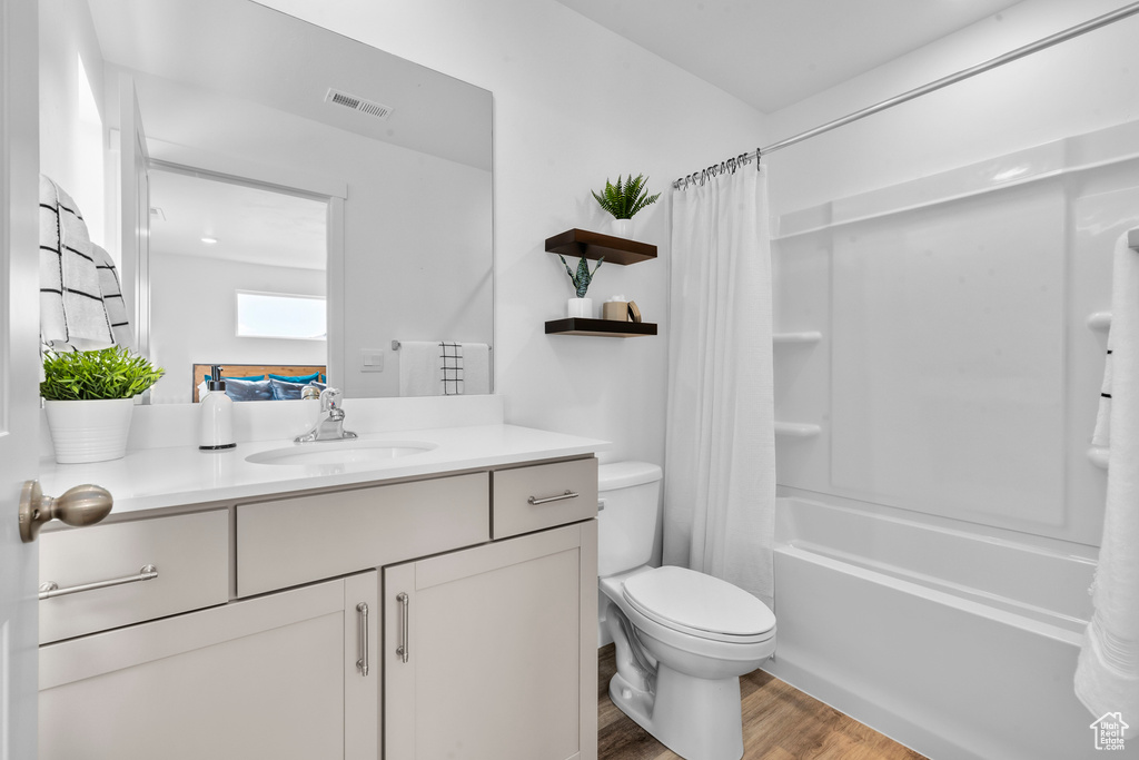 Full bath with vanity, shower / bathtub combination with curtain, wood finished floors, visible vents, and toilet