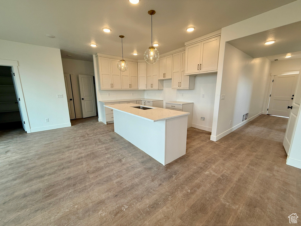 Kitchen with baseboards, pendant lighting, an island with sink, wood finished floors, and white cabinetry