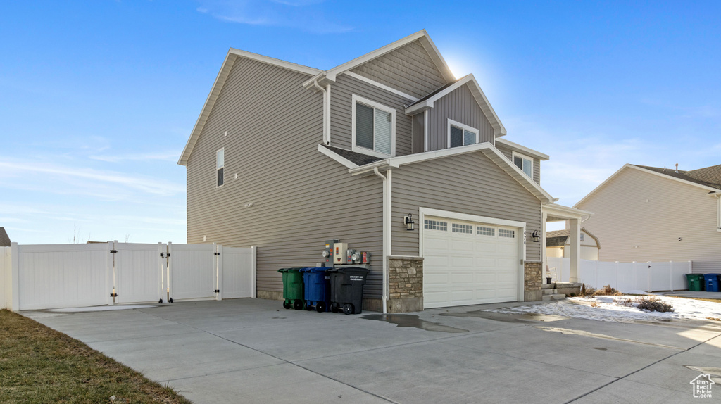 View of home\\\\\\\'s exterior featuring stone siding, an attached garage, concrete driveway, and a gate