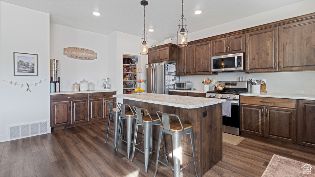 Kitchen with visible vents, a kitchen island, light countertops, appliances with stainless steel finishes, and dark wood-style floors