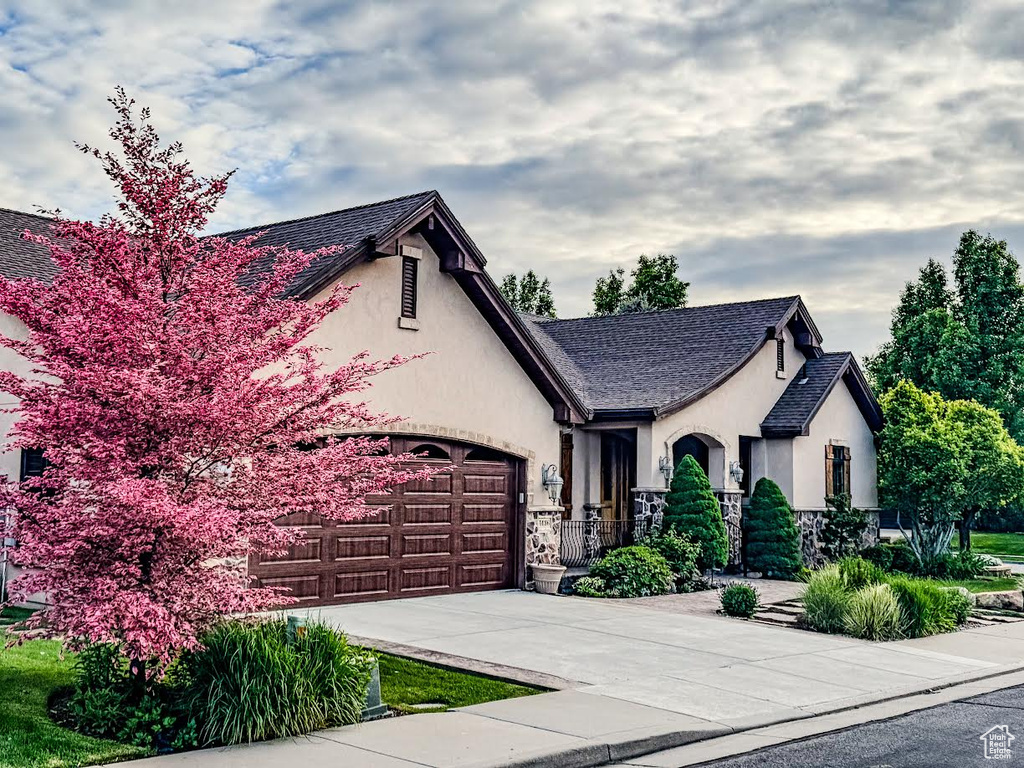 View of front of home with stucco siding, concrete driveway, stone siding, an attached garage, and fence
