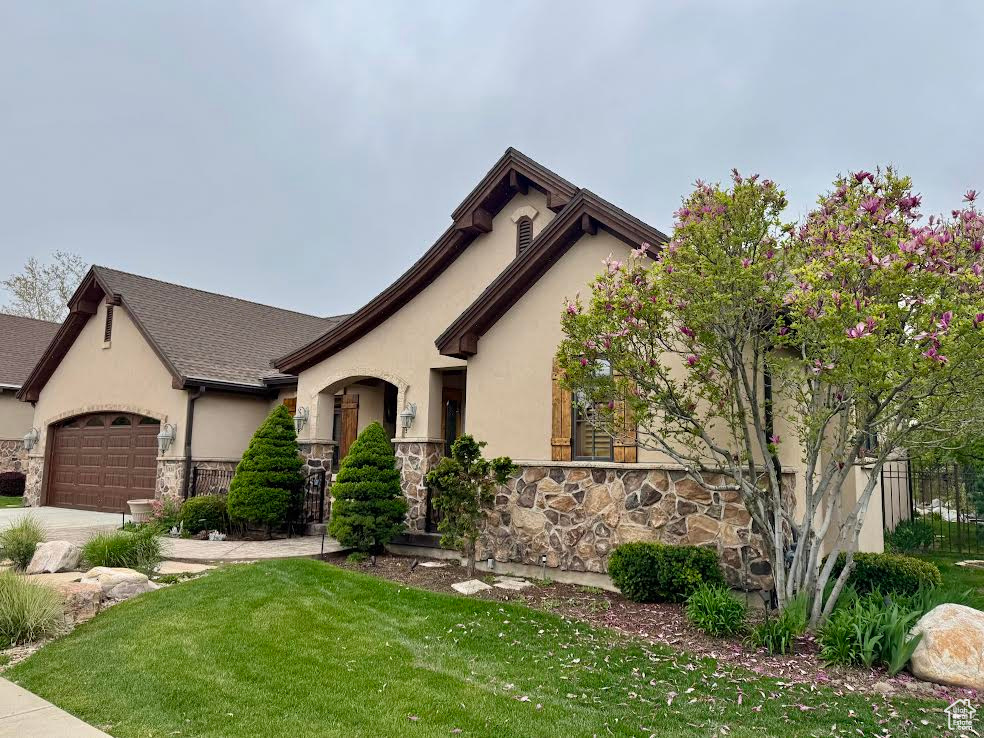 View of front of house featuring a front lawn, a garage, stone siding, concrete driveway, and stucco siding