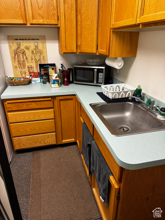 Kitchen featuring stainless steel microwave, light countertops, brown cabinets, and a sink