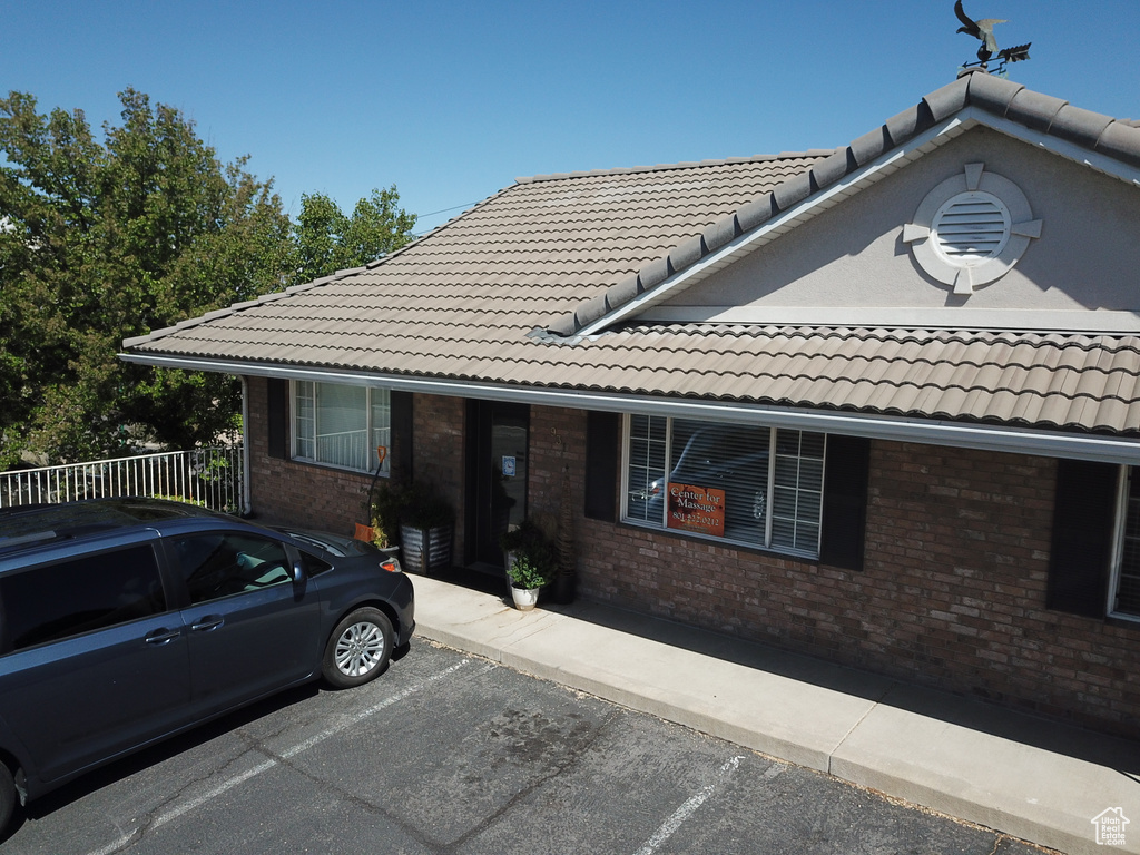 View of front of home with brick siding, uncovered parking, fence, and a tile roof